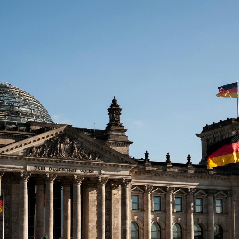 Historic Reichstag building in Berlin with prominent German flags displayed under a clear blue sky.