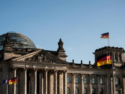 Historic Reichstag building in Berlin with prominent German flags displayed under a clear blue sky.
