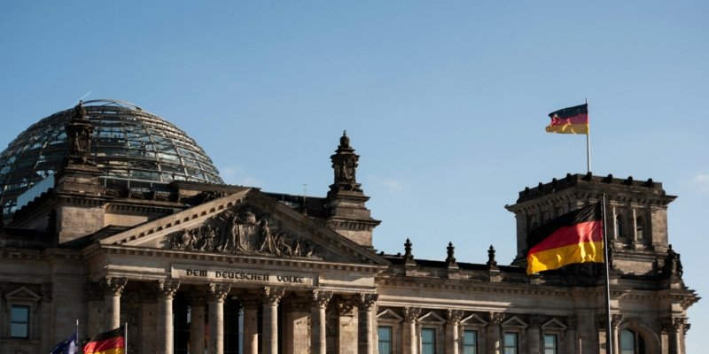 Historic Reichstag building in Berlin with prominent German flags displayed under a clear blue sky.
