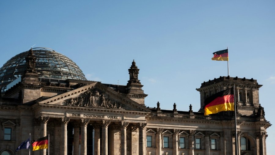 Historic Reichstag building in Berlin with prominent German flags displayed under a clear blue sky.